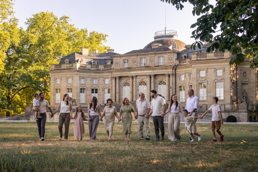 Großfamilie spaziert händehaltend im Grünen vor dem Schloss Monrepos in Ludwigsburg