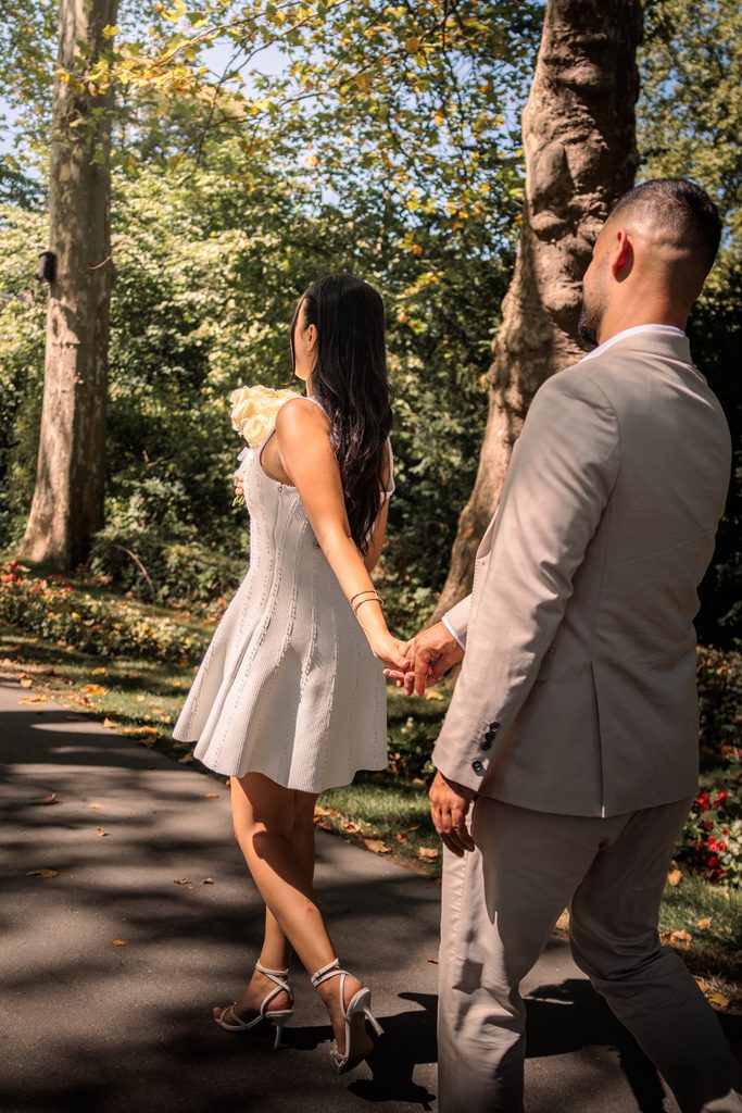 Braut führt Bräutigam bei Fotoshooting durch eine Allee