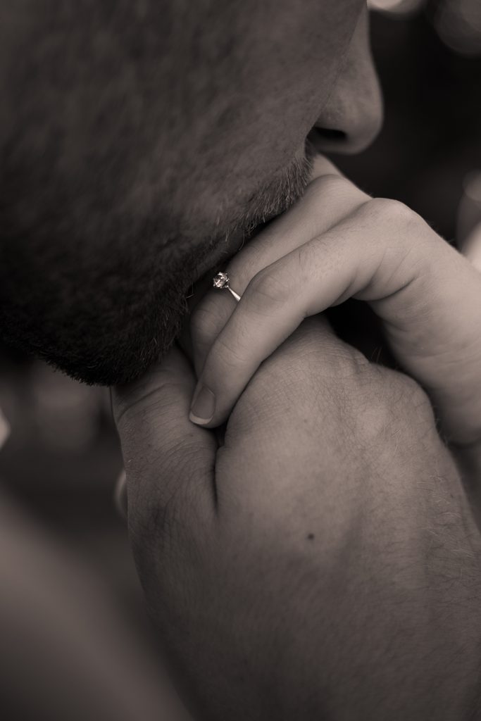 Detailaufnahme eines Mannes, der liebevoll die Hand und den Verlobungsring seiner Partnerin küsst