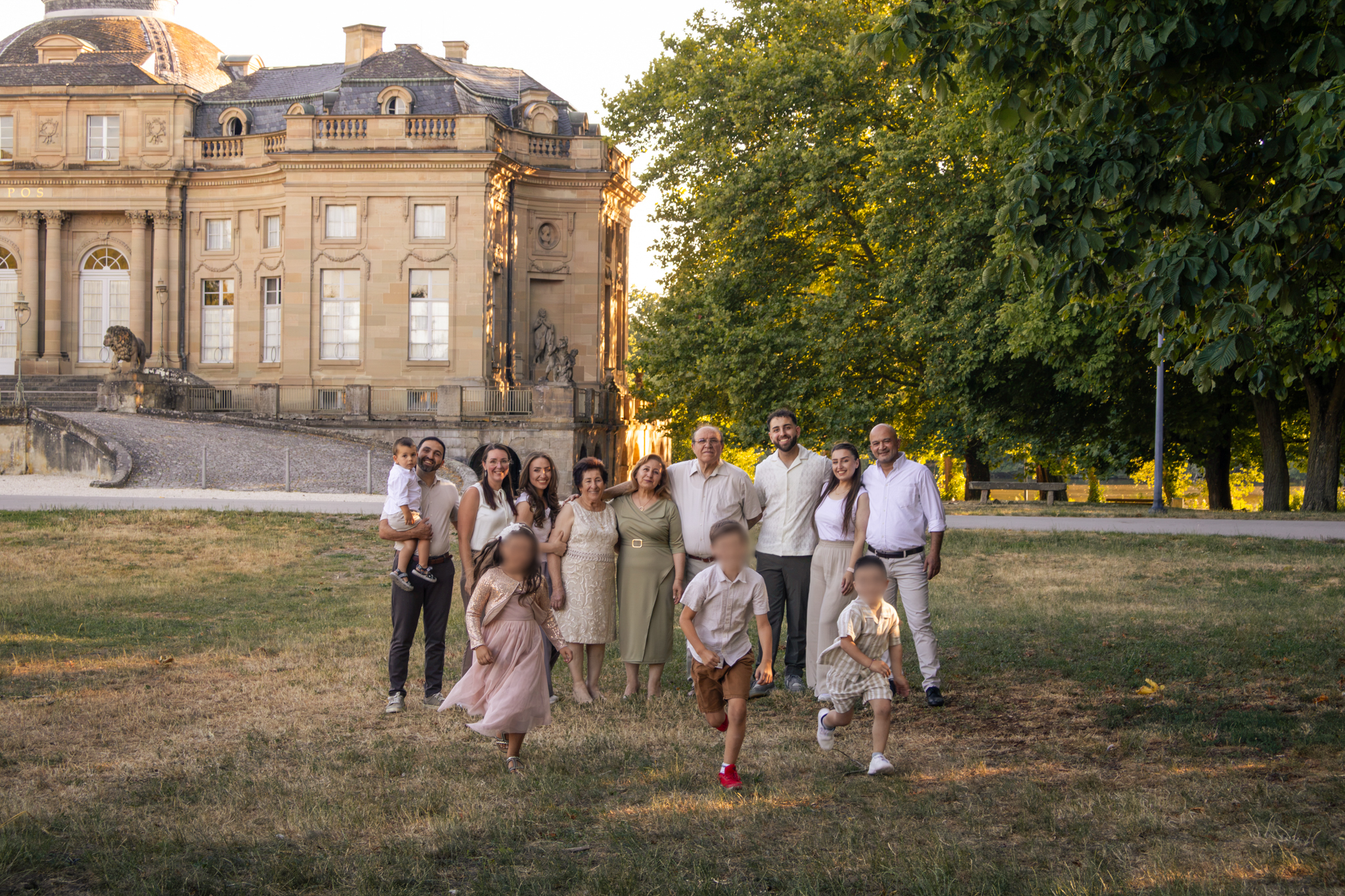 Mehrgenerationenfamilie umarmt sich in der Abendsonne, während die Kinder spielen
