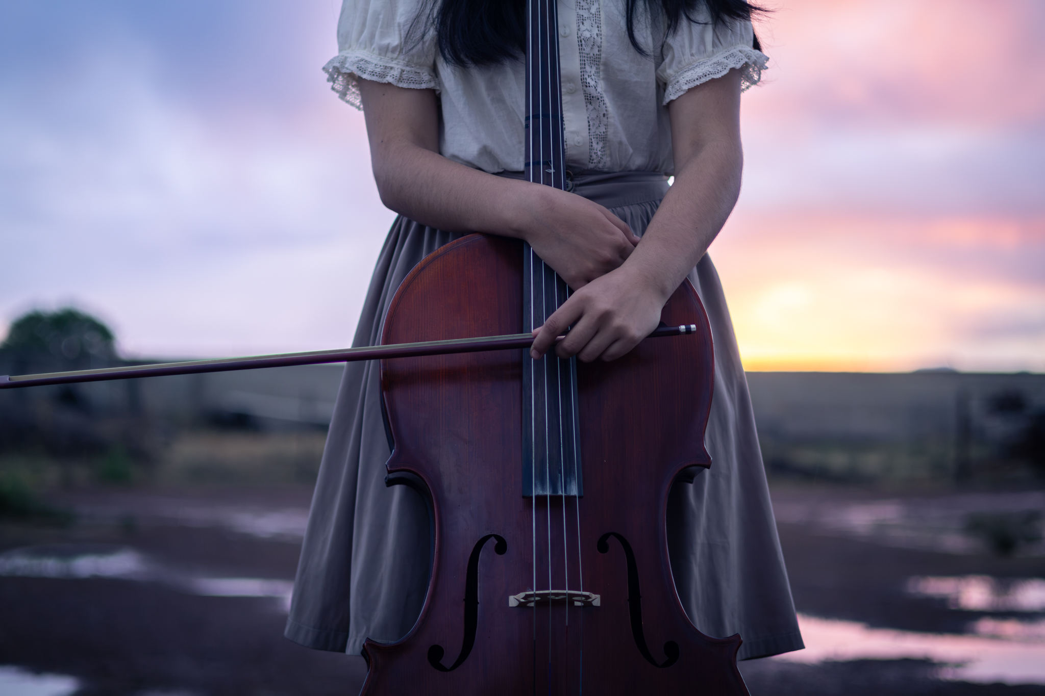 Mädchen hält ihr Cello vor dem Sonnenuntergang