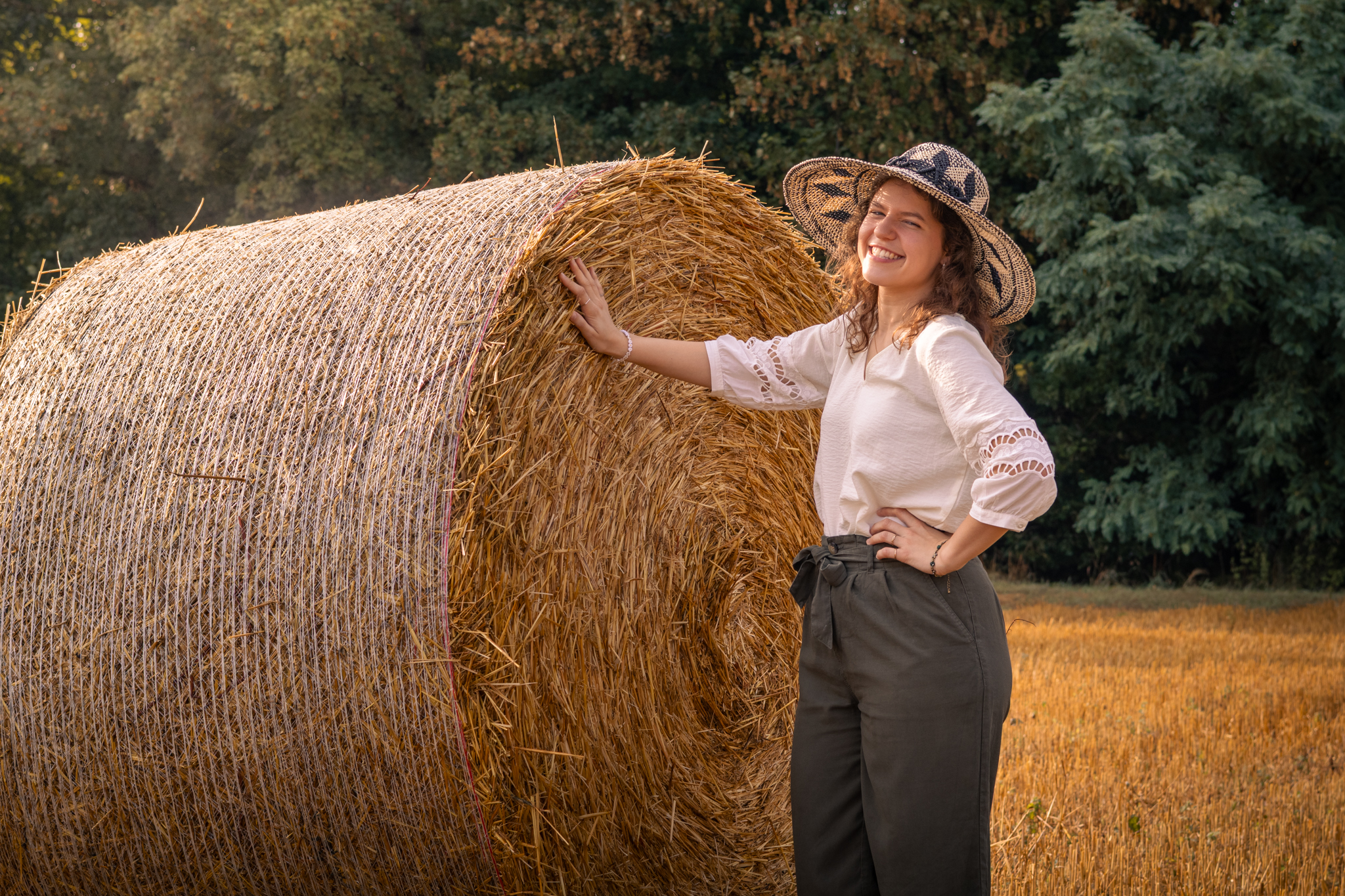 Frau mit Sonnenhut posiert strahlend neben einem großen Heuballen
