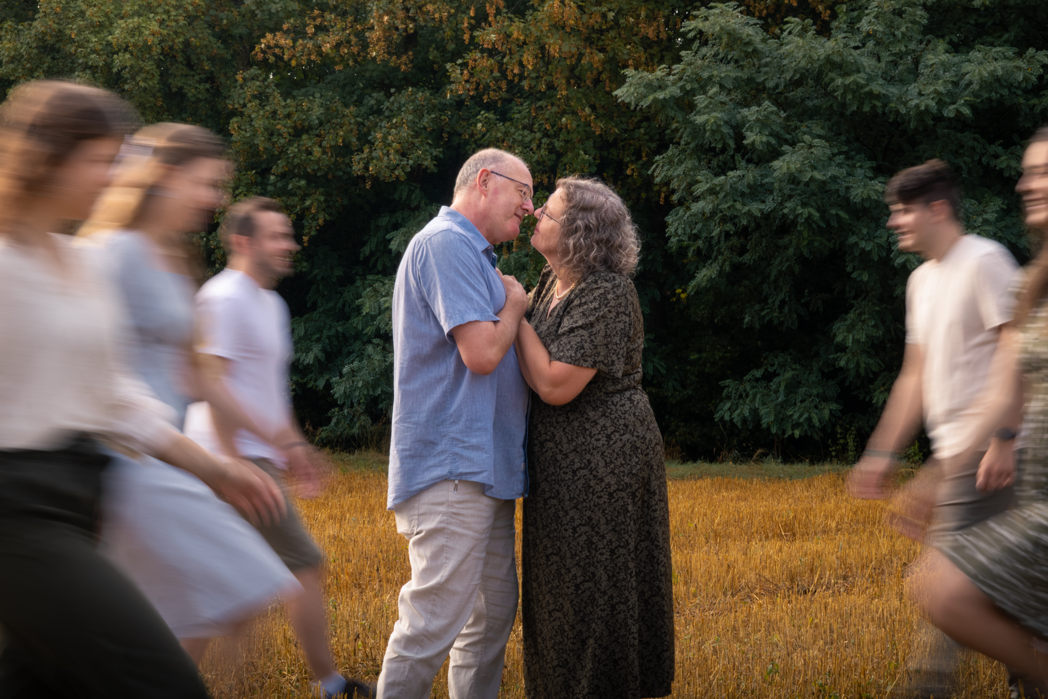 Älteres Paar küsst sich liebevoll, während Familienmitglieder vorbeigehen